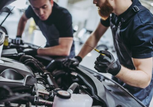 Two men mechanics working on engine of car with bonnet open